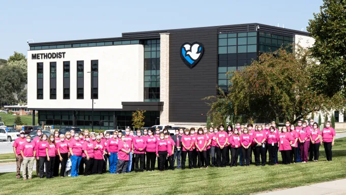 A large group of people wearing pink shirts stand in a line on the lawn of the Methodist Jennie Edmundson Hospital.